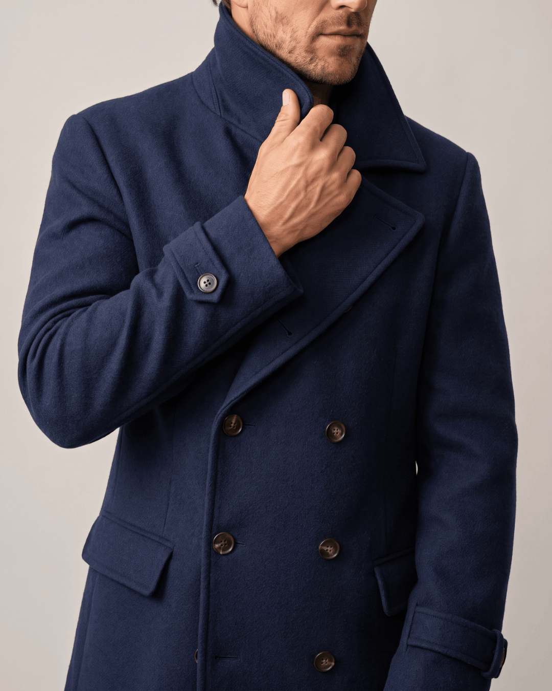 Navy blue wool coat showing double-breasted buttons, flap pocket and button cuff tab