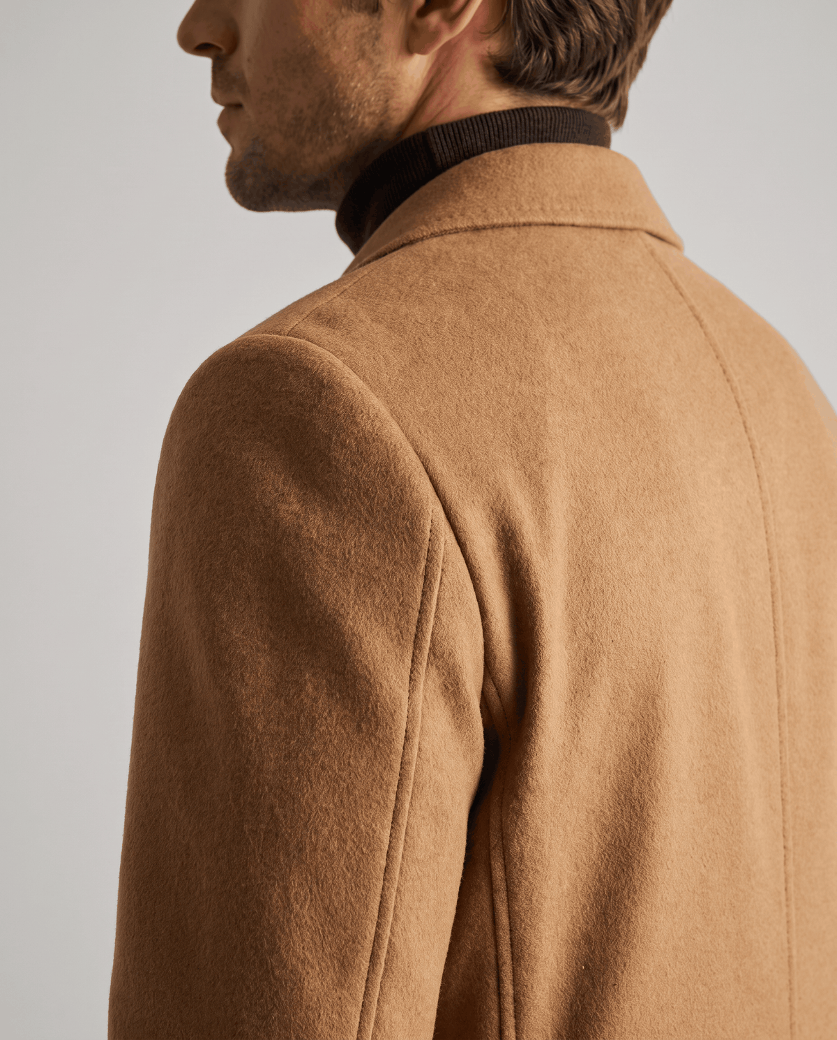 Shoulder and sleeve detail of a brown wool coat with a smooth, textured finish