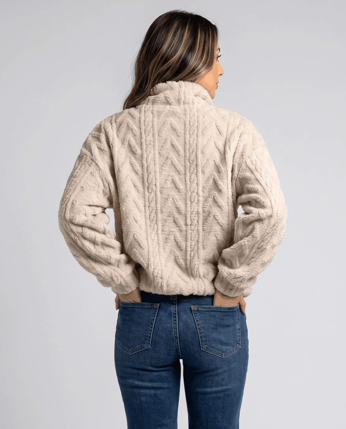 Back view of cream cable fleece pullover worn with medium wash jeans