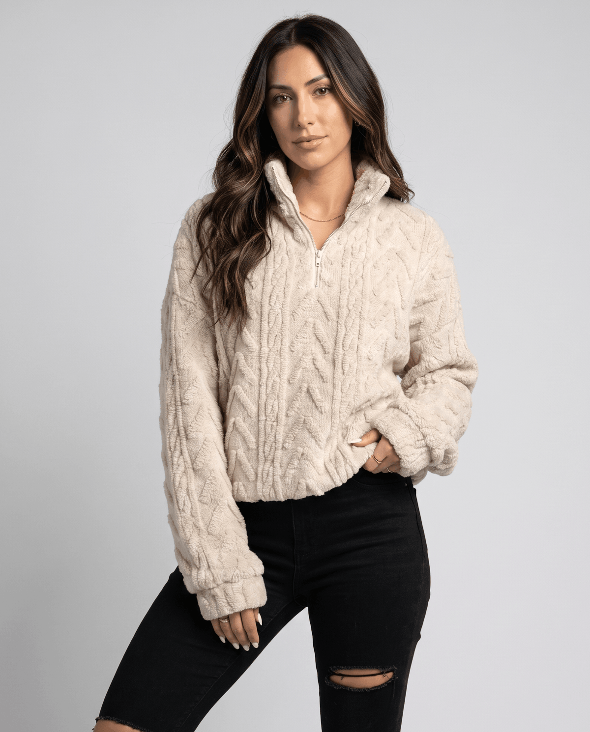 Woman wearing a cream cable-knit fleece quarter-zip pullover with black ripped jeans