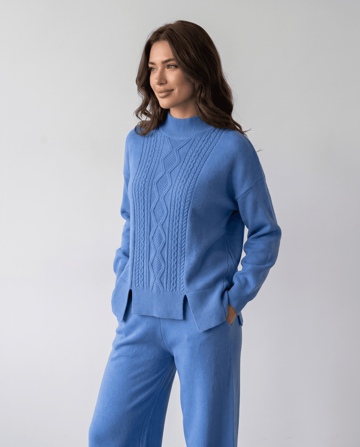 Blue cable knit pullover with hands in the pants pockets, front view