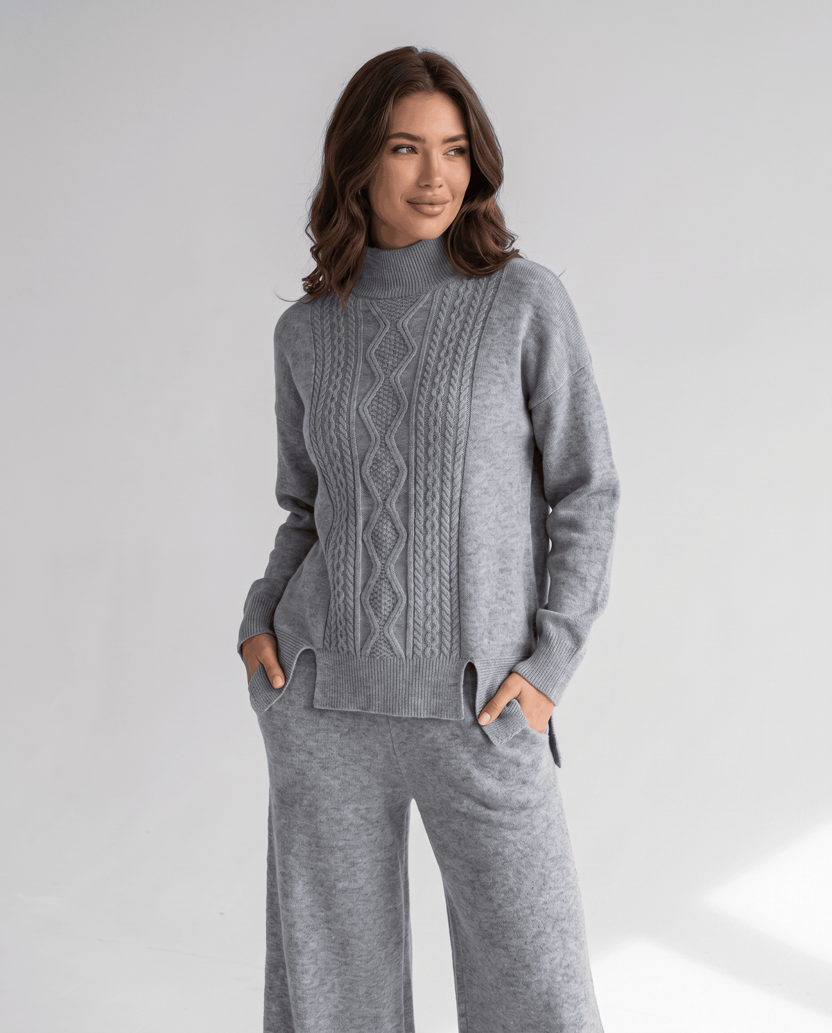 Grey cable knit pullover with hands in the pants pockets, front view