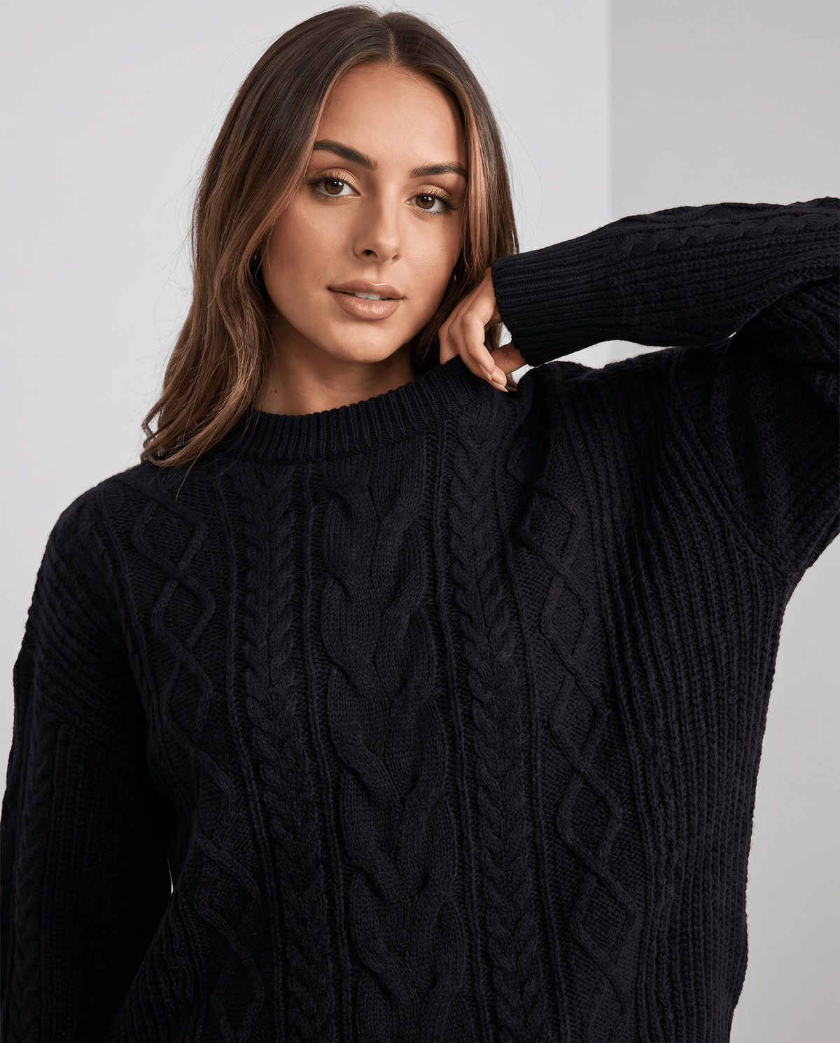 Close-up of woman in black cable knit crew neck sweater with arm raised