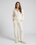 Woman wearing an off-white cable-knit zip-up loungewear set with matching wide-leg pants, hands in pockets