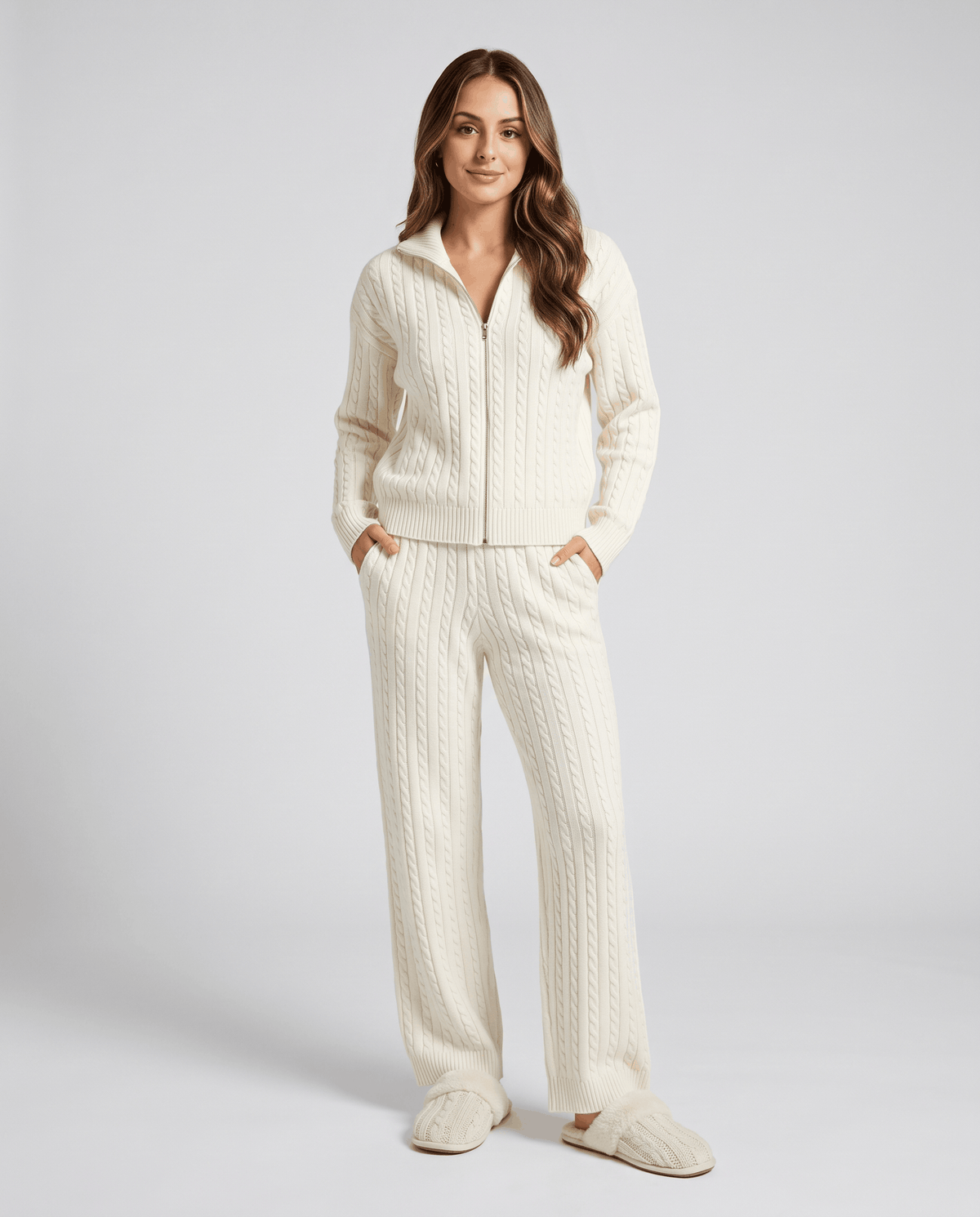 Woman wearing an off-white cable-knit zip-up loungewear set with matching wide-leg pants, hands in pockets