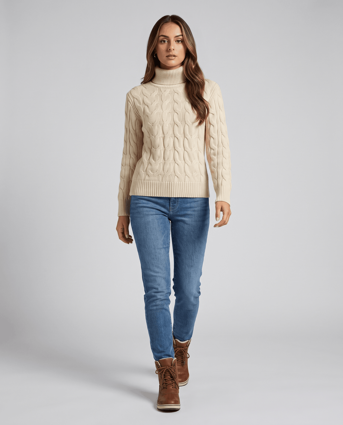 Beige cable sweater worn with light jeans and brown boots, full-length view