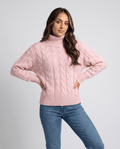 Woman wearing a pink cable knit turtleneck pullover sweater with blue jeans, hands on hips