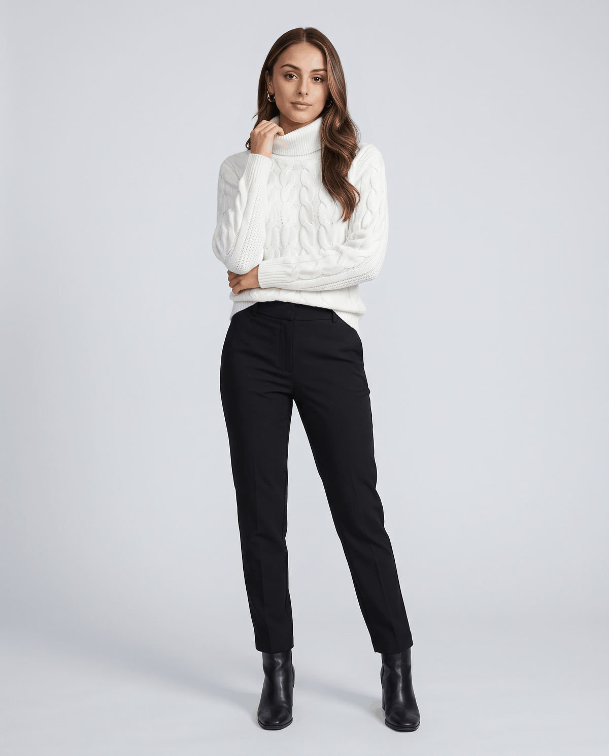 White cable turtleneck sweater with black trousers and ankle boots, full-length view