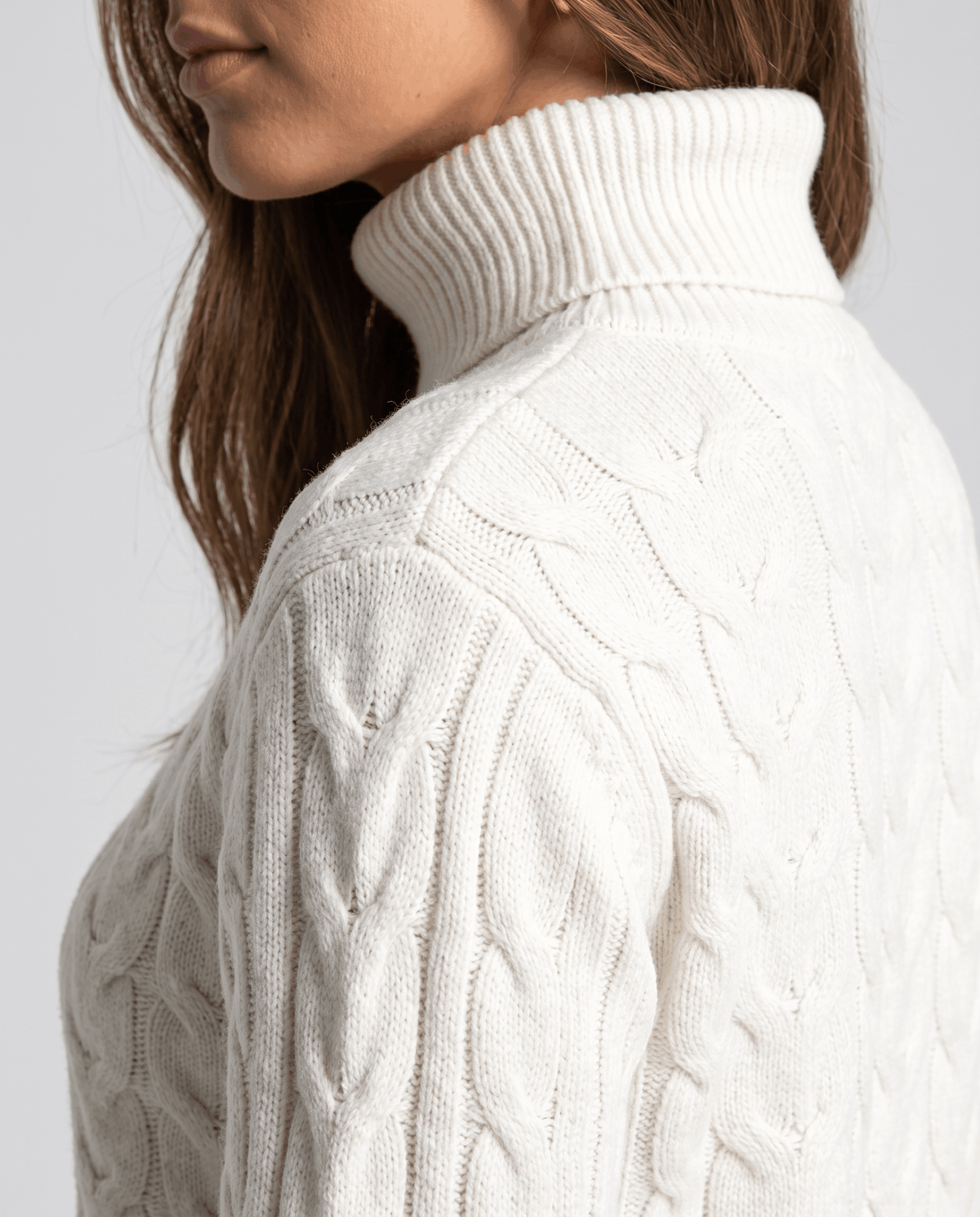 Side close-up of the white fold-over neck and cable-knit sleeve texture