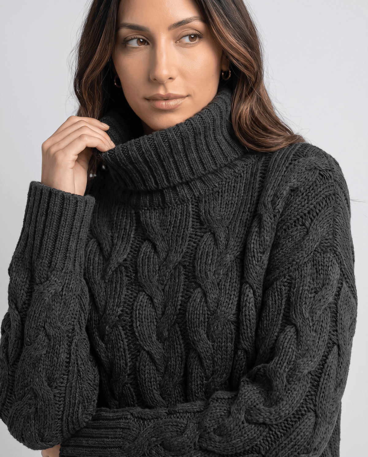 Model adjusting the ribbed collar of a charcoal black chunky turtleneck