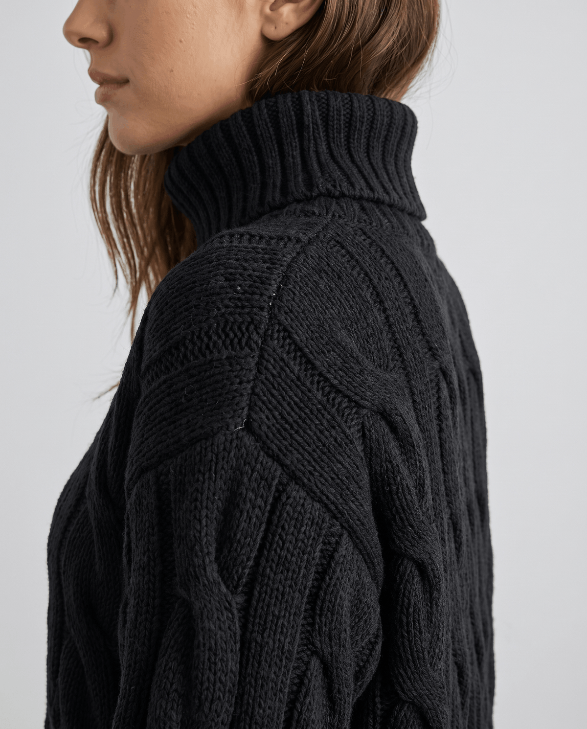 Side shoulder detail of black cable knit sweater with folded turtleneck