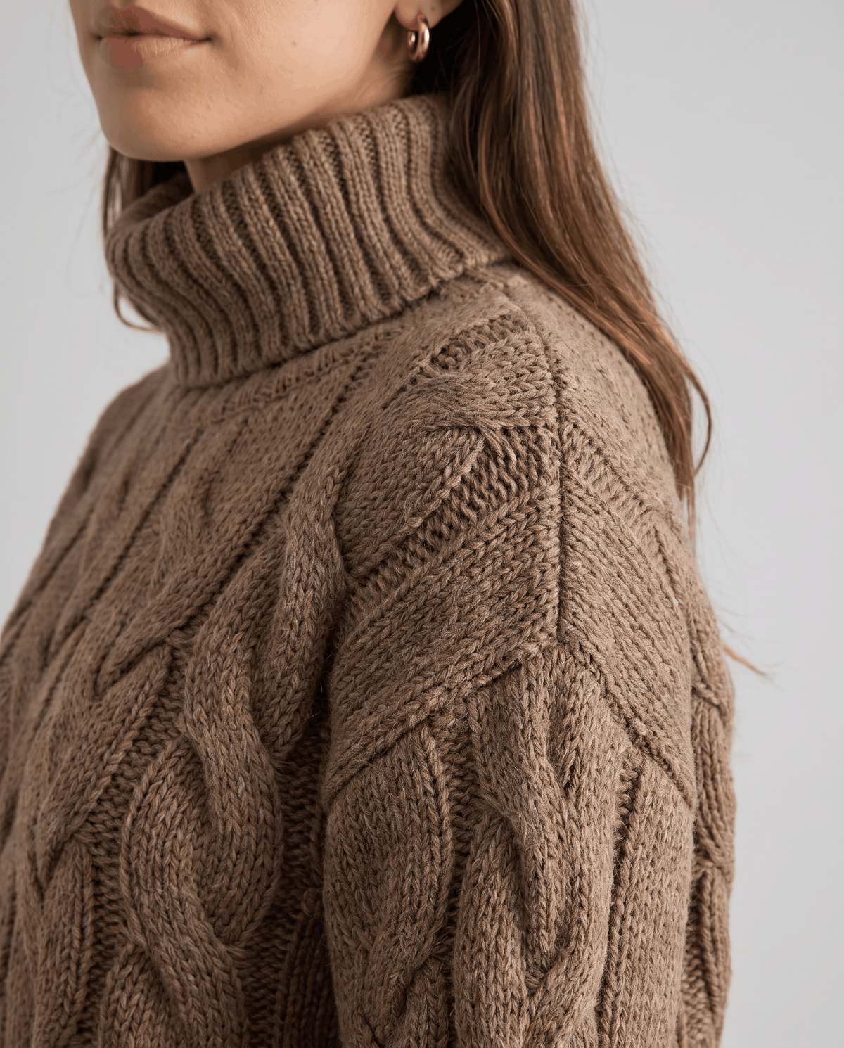 Close-up of ribbed turtleneck and braided cables on a brown knit sweater