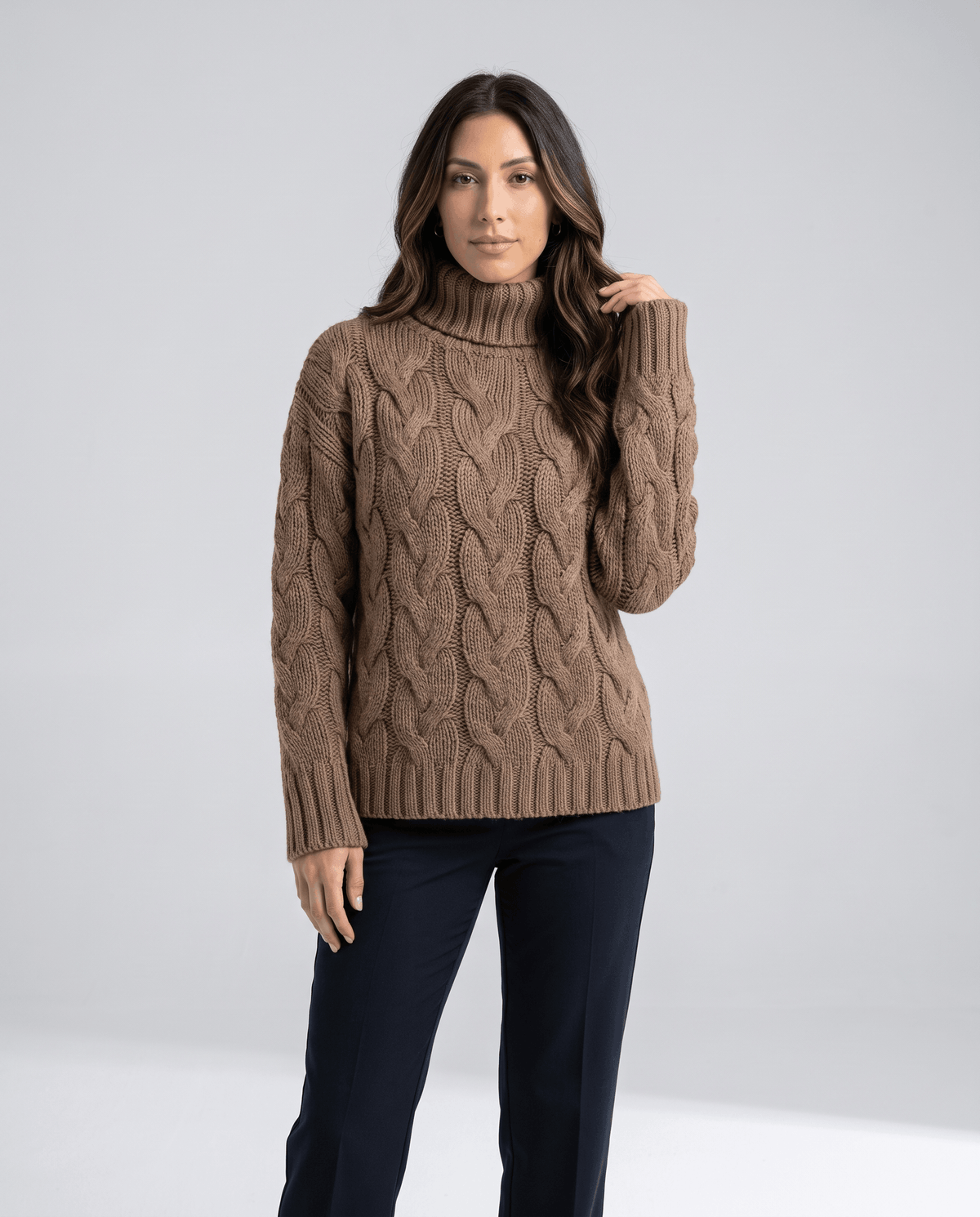 Woman wearing a brown chunky cable knit turtleneck sweater with black pants