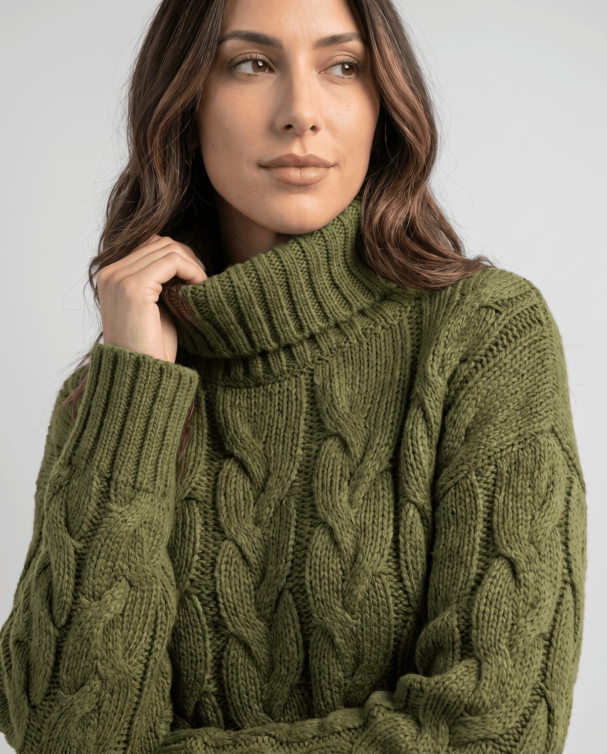 Model touching the collar of an olive green chunky turtleneck sweater