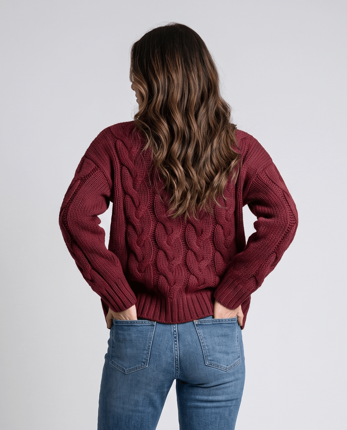 Back view of burgundy cable knit sweater tucked into light wash jeans