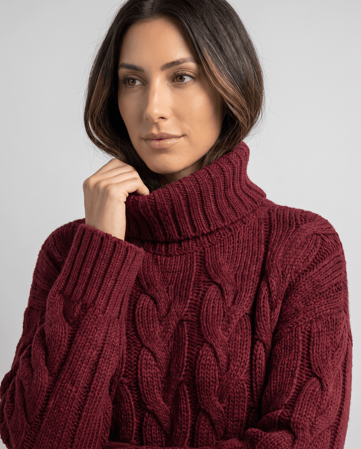 Model touching the folded collar of a burgundy chunky turtleneck