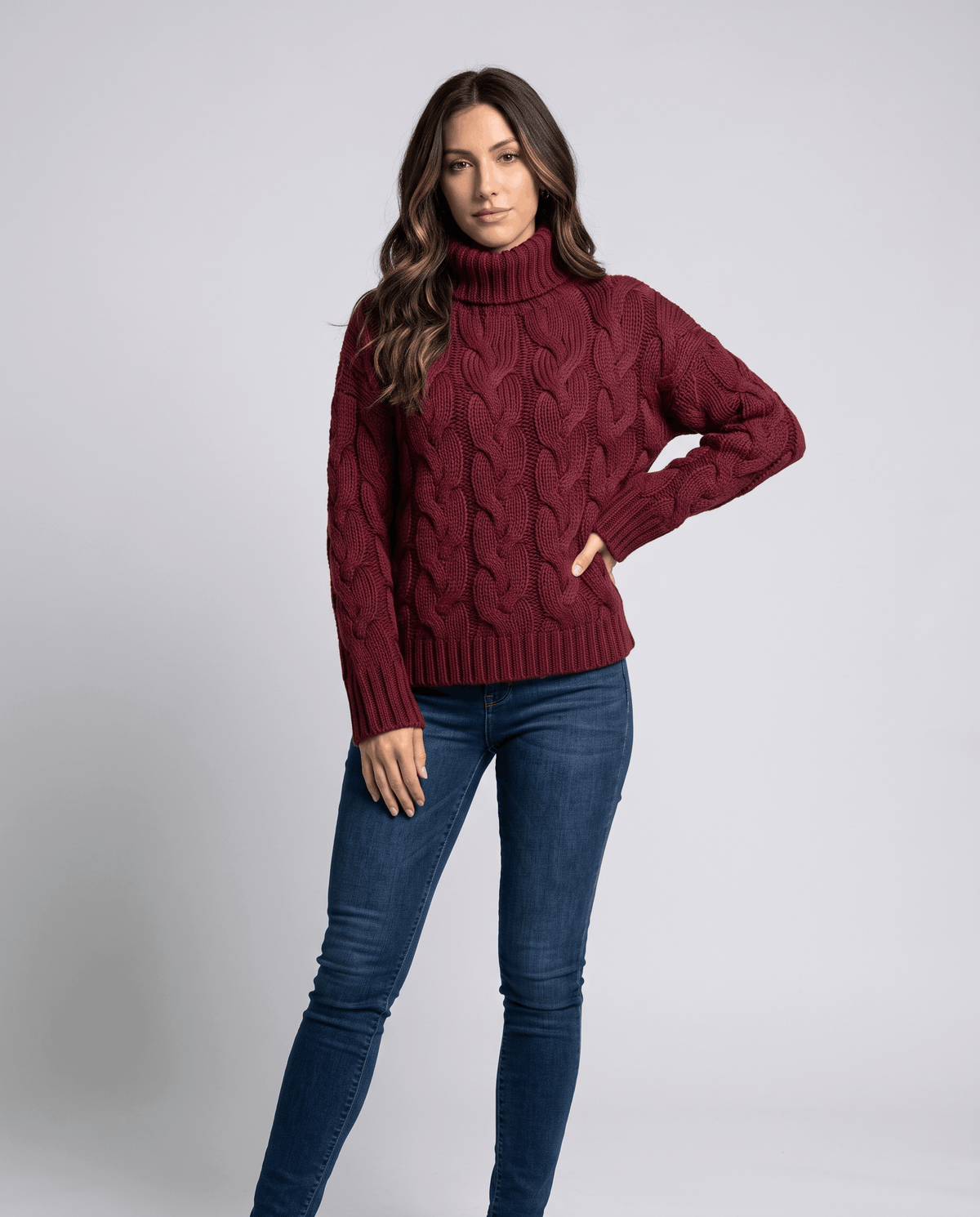 Front view of burgundy red cable knit turtleneck worn with medium wash jeans