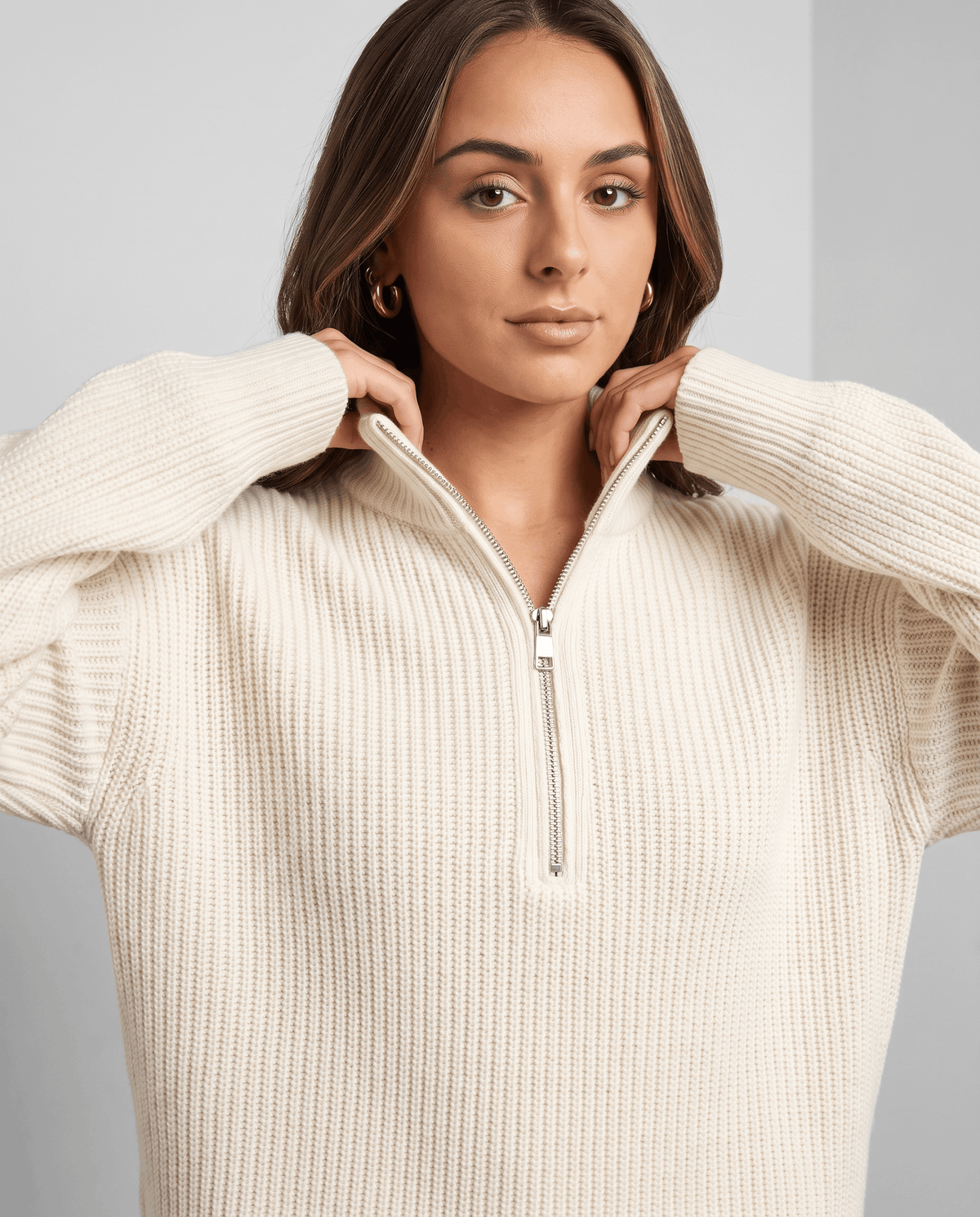 Model holding the stand collar of a white chunky knit sweater