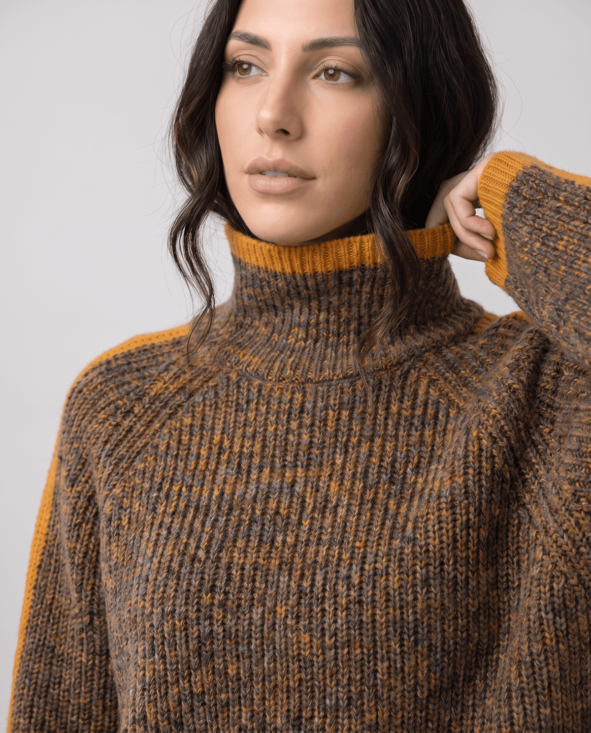 Close-up of model touching the mustard-trimmed ribbed turtleneck on a marled brown knit