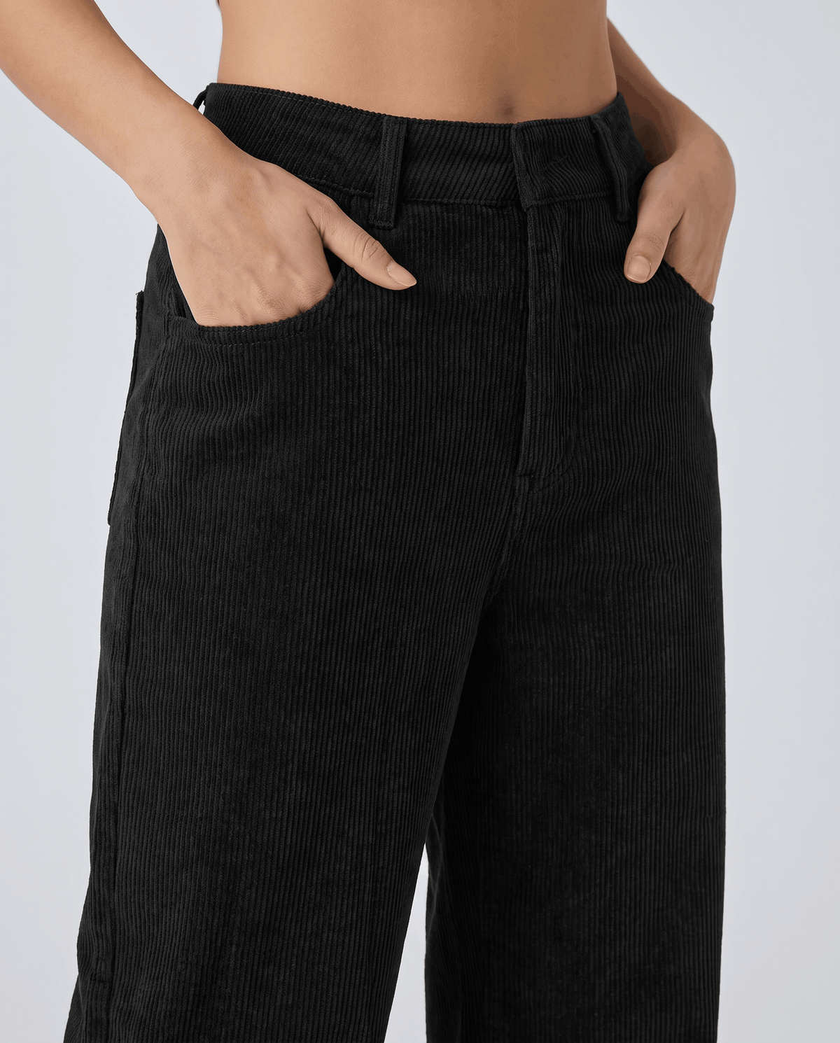 Close-up of black ribbed fabric at the button waist with hands in the front pockets