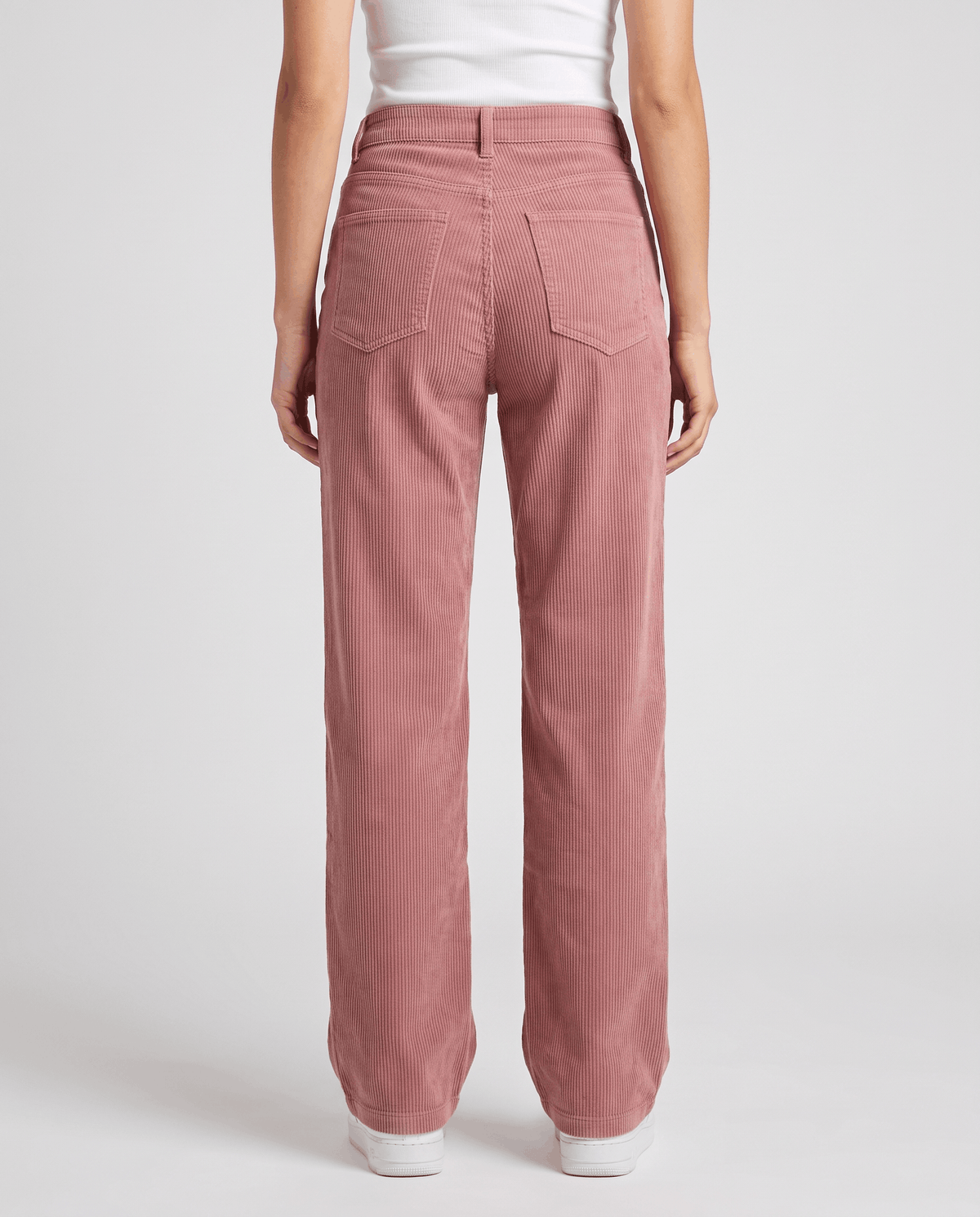 Back view of rose pink ribbed trousers with back patch pockets and white sneakers