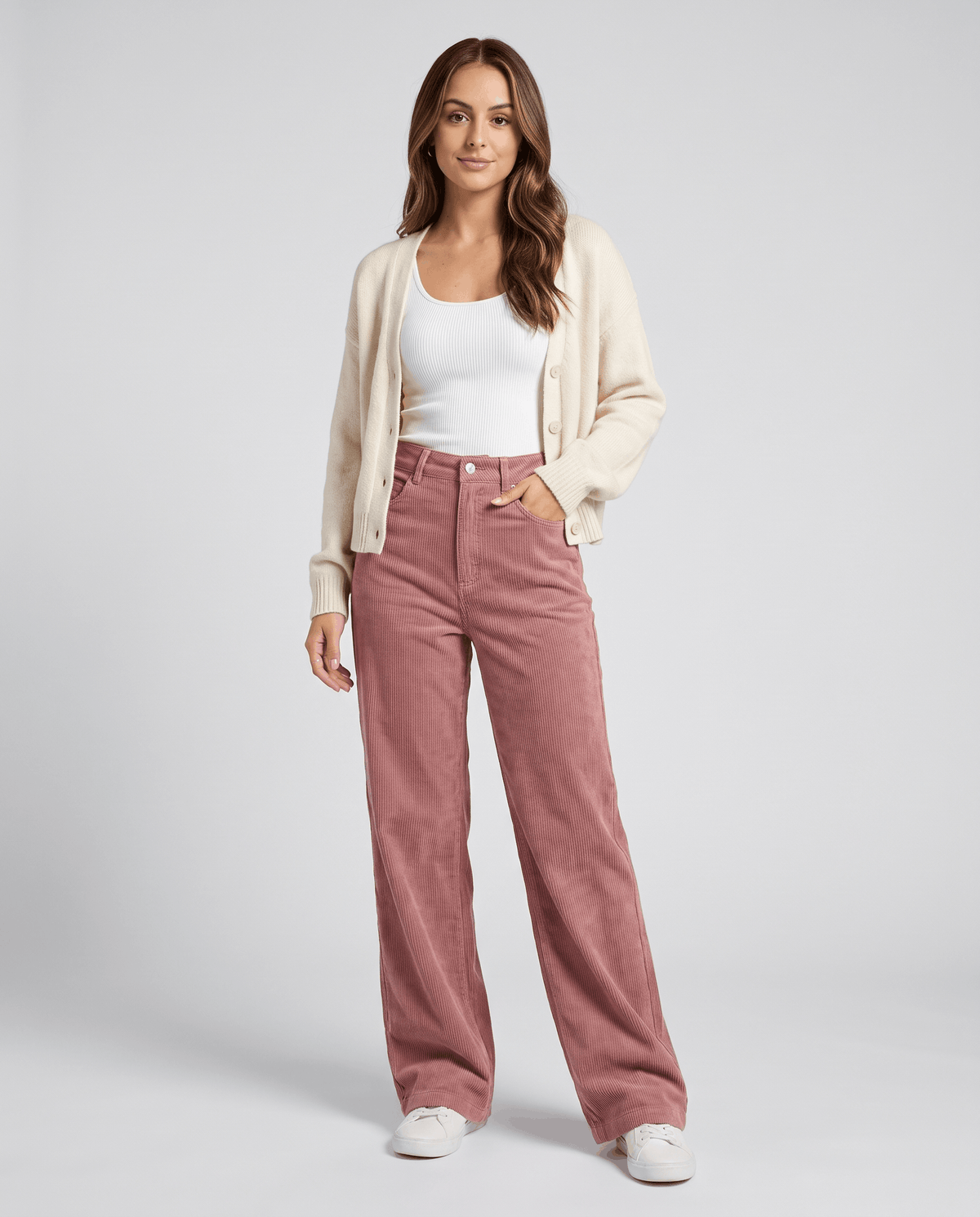Model in pink corduroy trousers styled with a cream cardigan, white tee and sneakers
