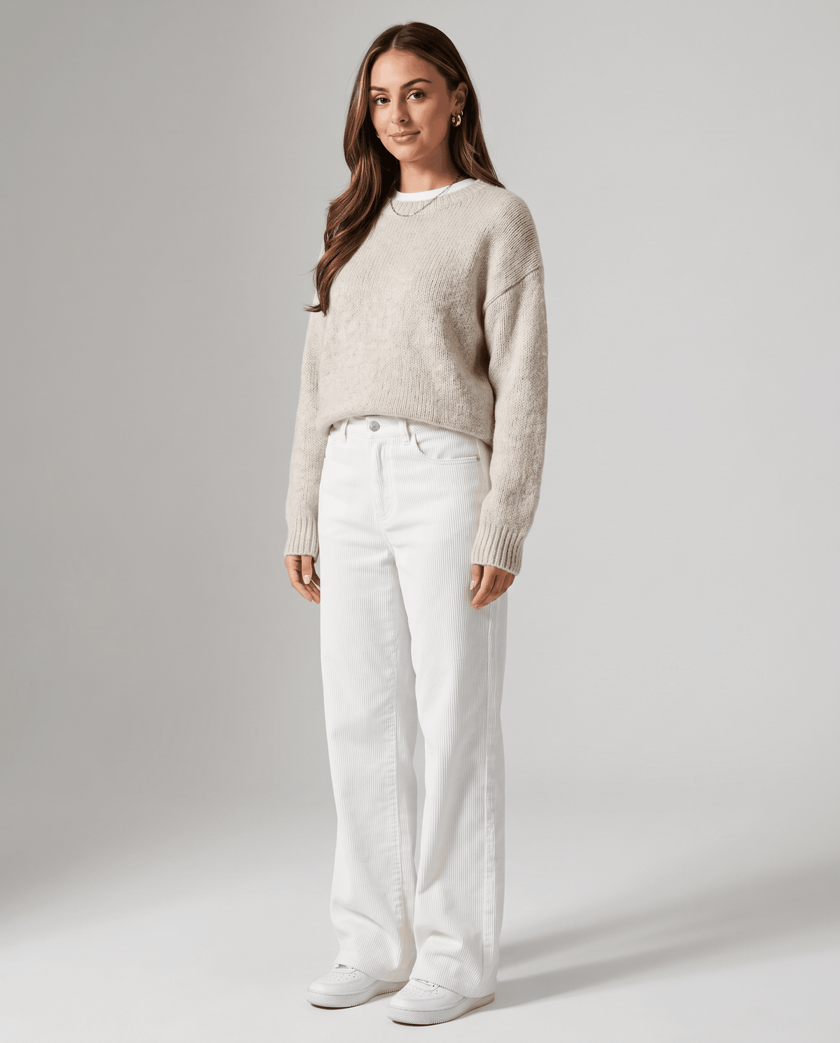 Model in cream ribbed trousers styled with an oatmeal knit sweater and white sneakers