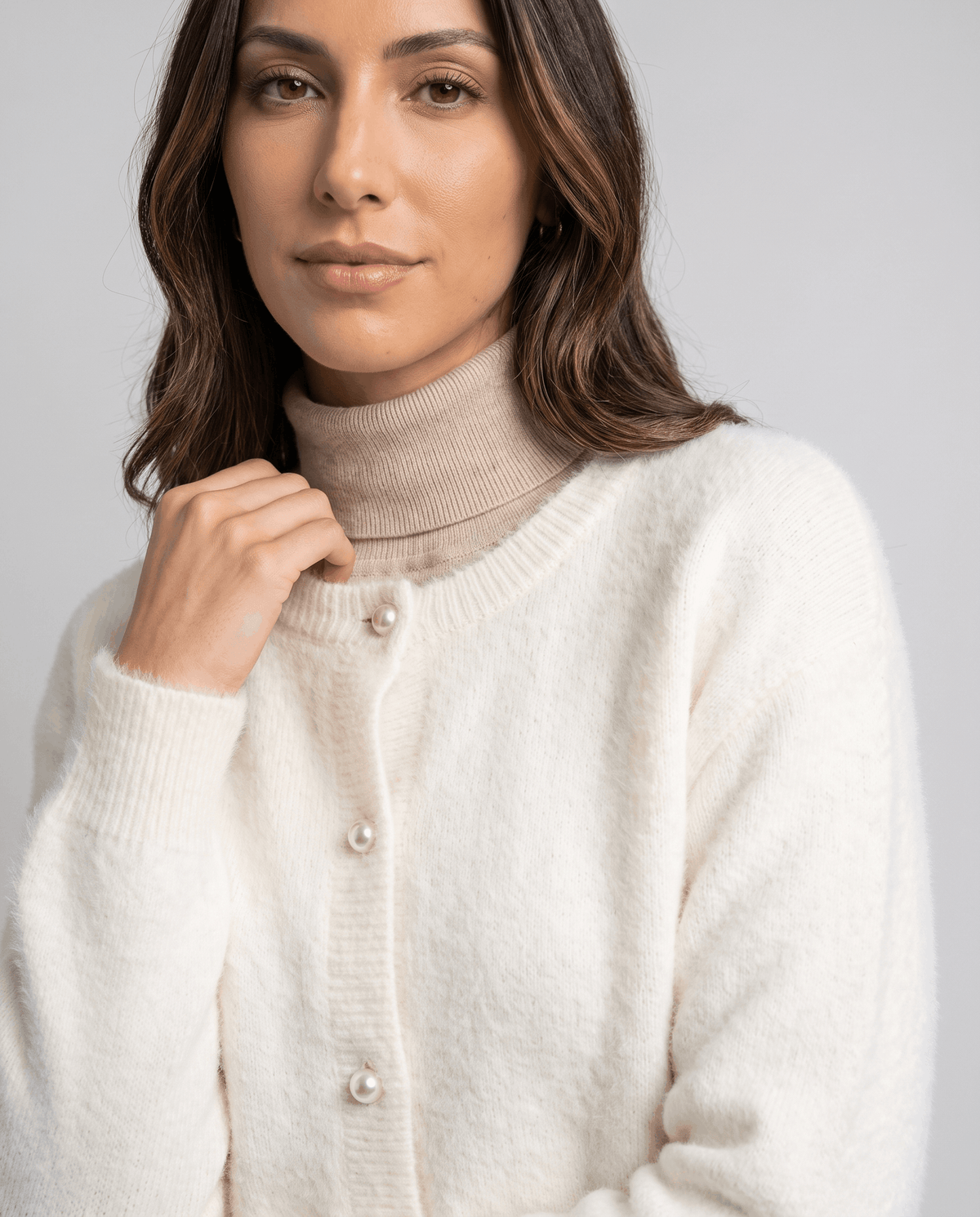 Detail of the pearl buttons on the beige cardigan with a hand at the collar