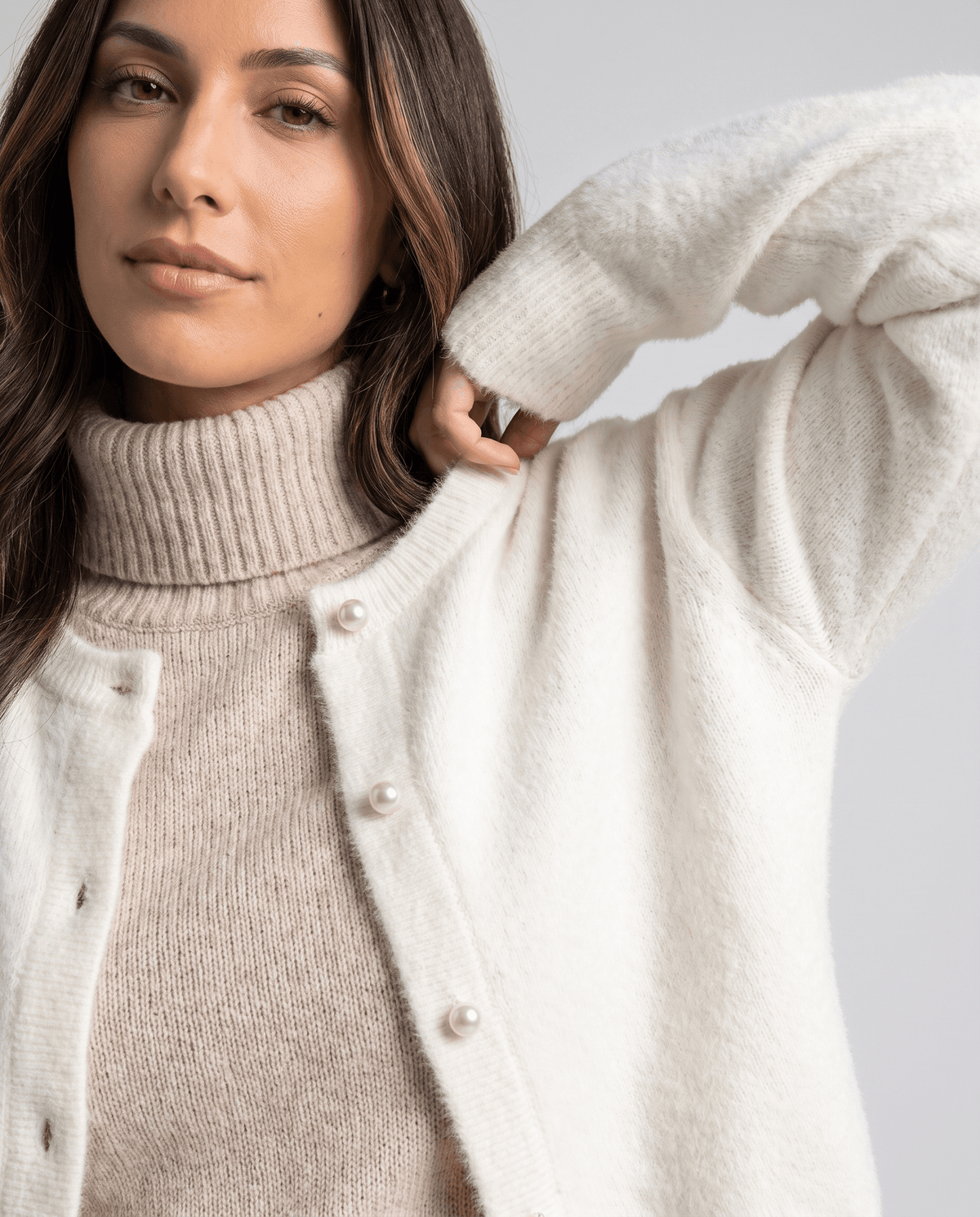 Close-up of the beige cardigan over a turtleneck with a hand at the shoulder