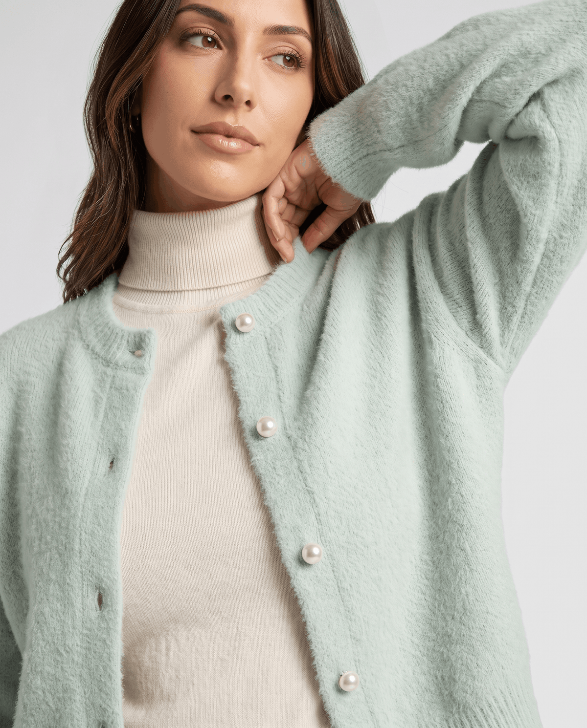 Close-up of the green cardigan over a cream turtleneck with a hand raised