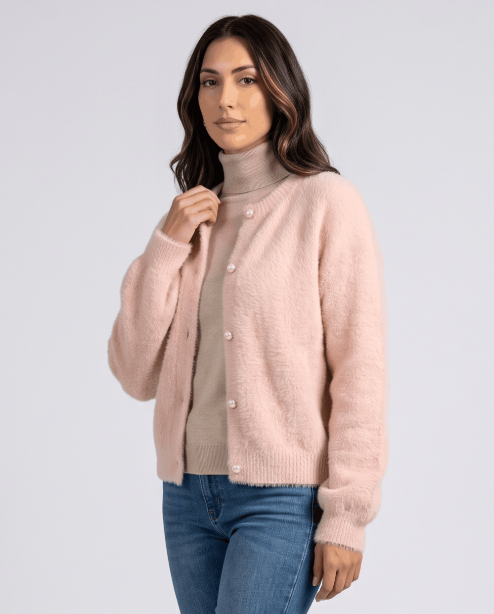 Pink cardigan over a taupe turtleneck with jeans and a hand at the collar