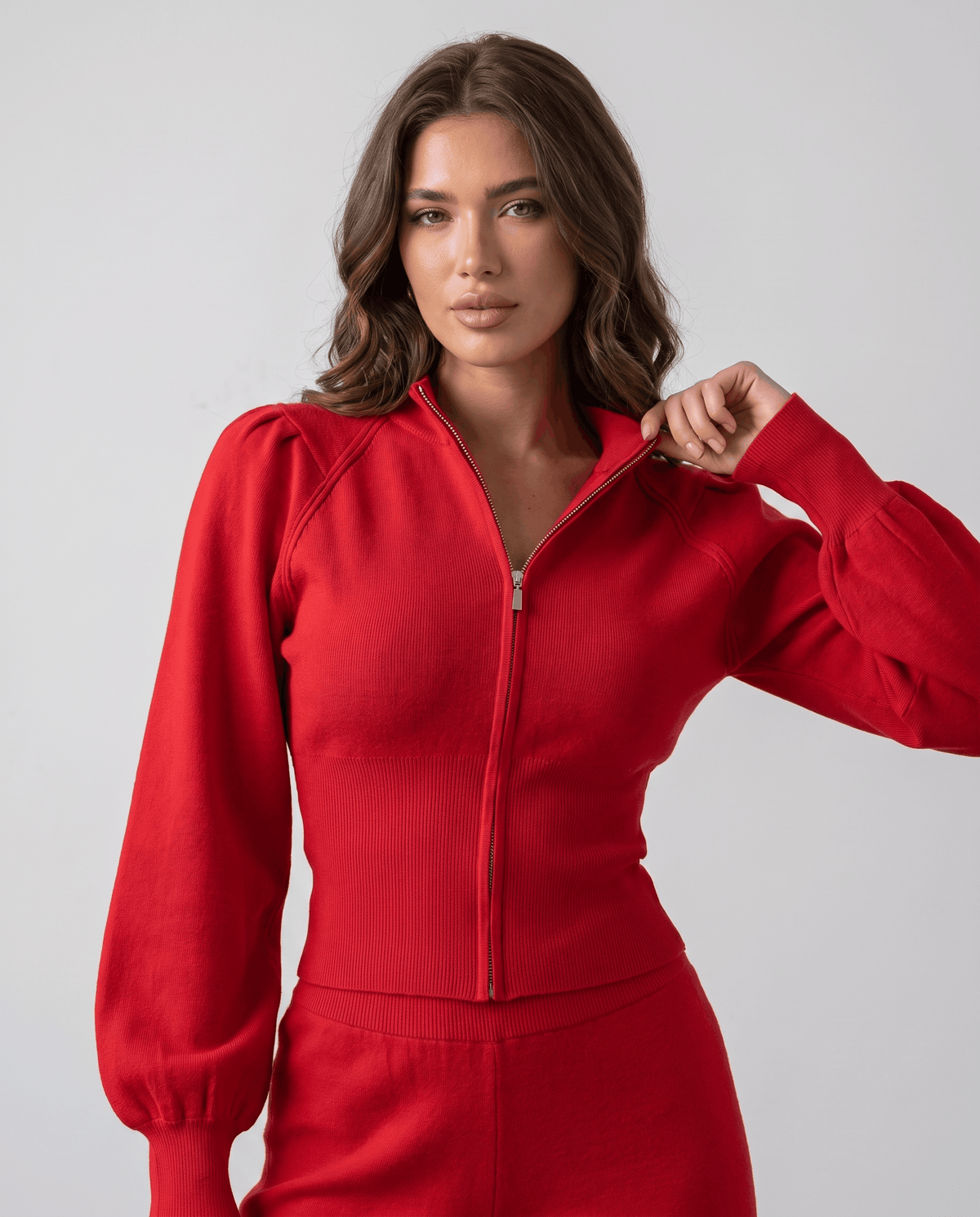 Close-up of the zip, stand collar and puffed ribbed-cuff sleeve on the red knit top