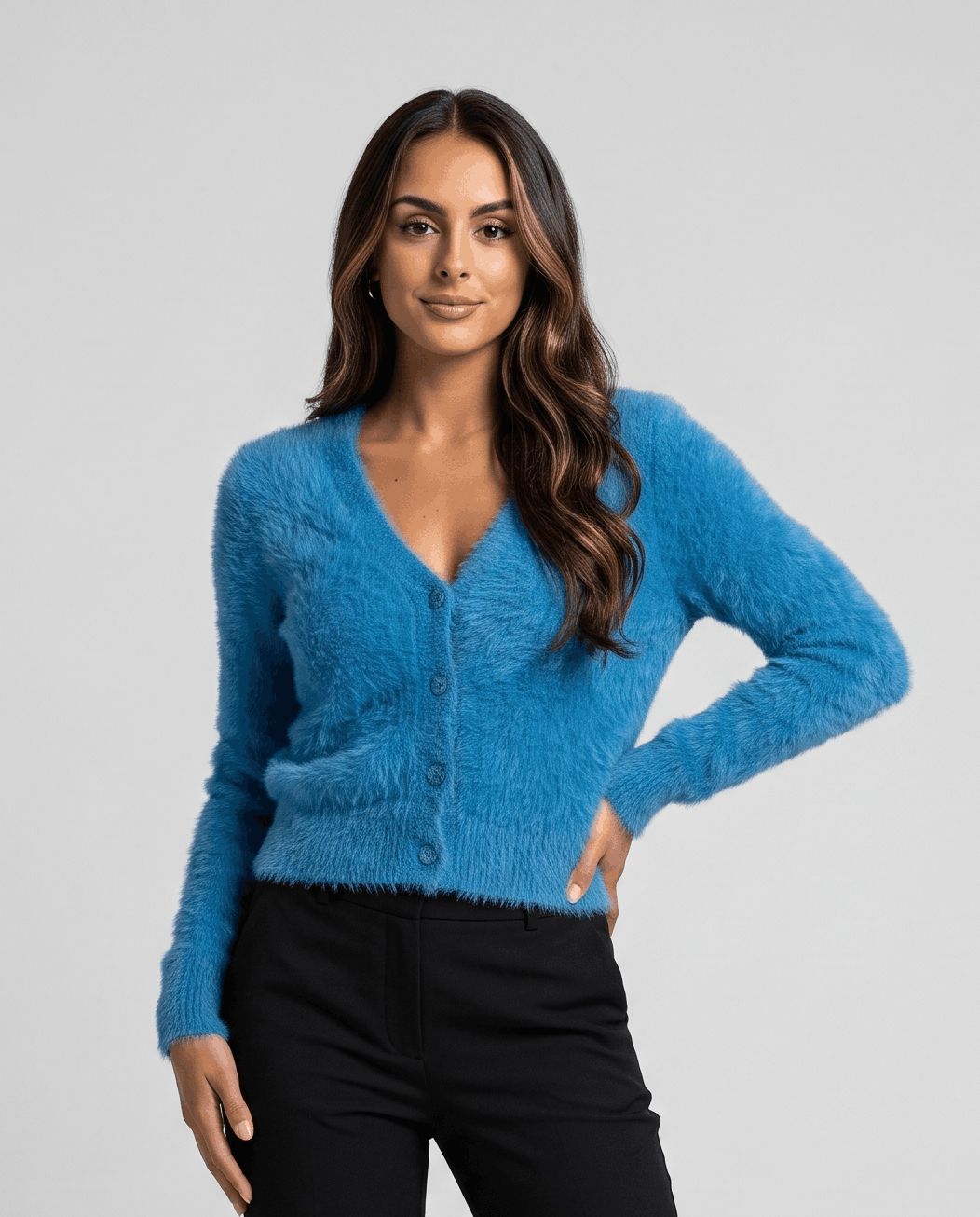 Blue cardigan buttoned up with black trousers and a hand on the hip
