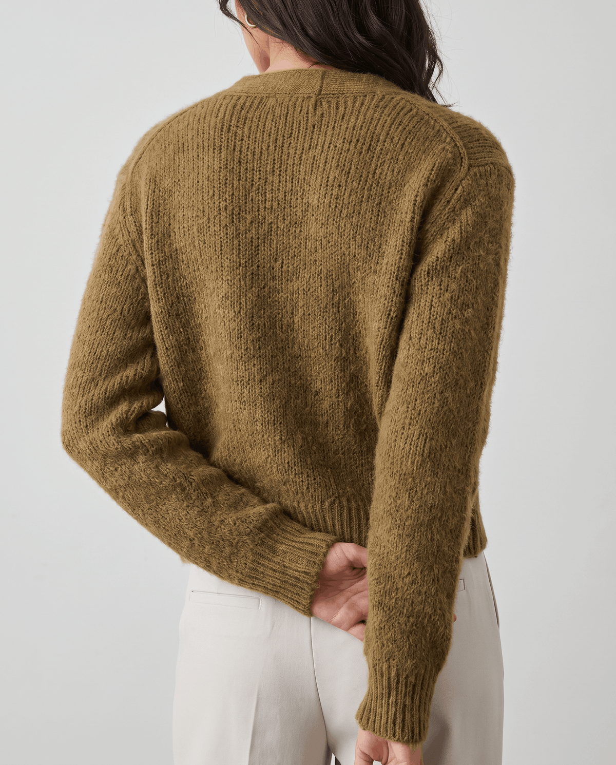Back view of the olive green cardigan worn with cream trousers
