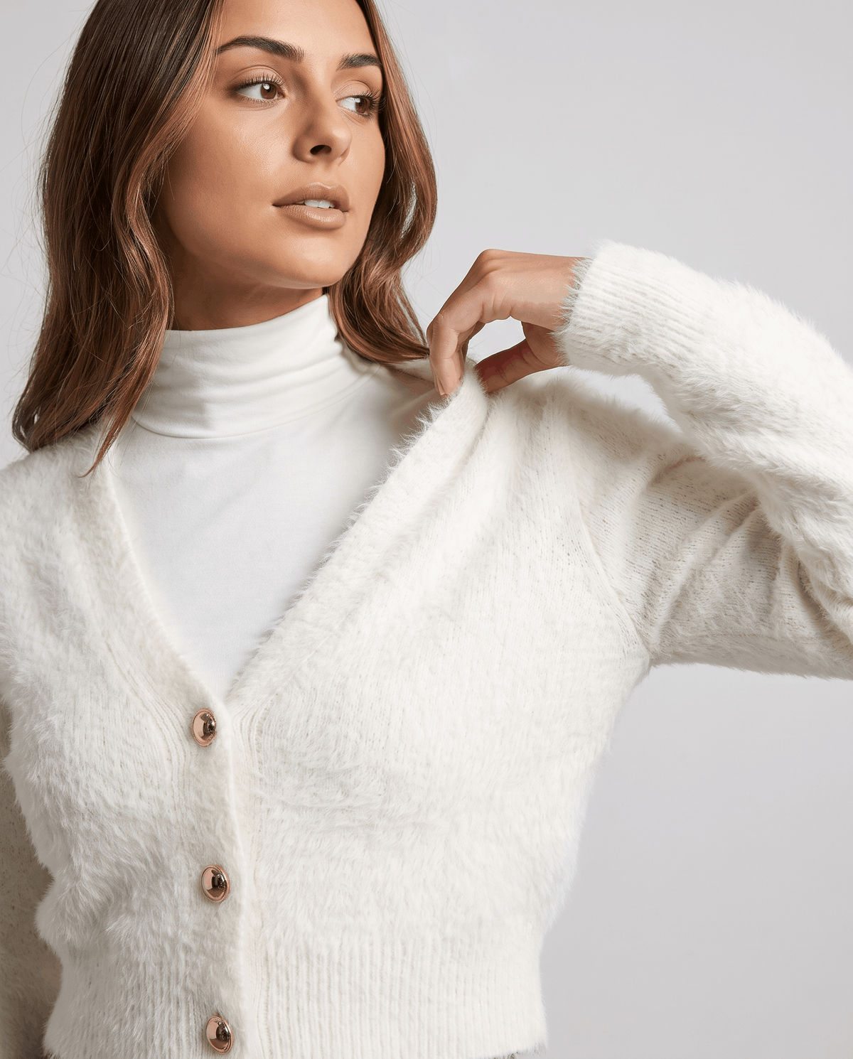 White cardigan close-up with a hand at the collar and a white turtleneck underneath