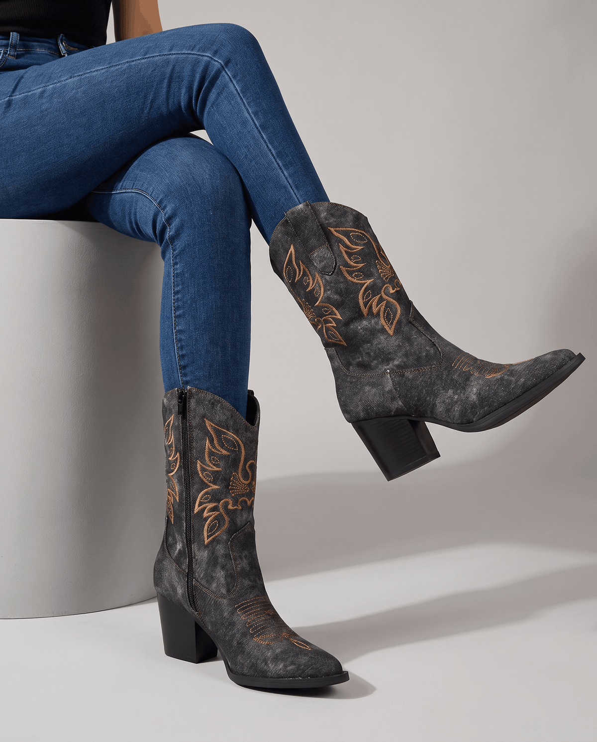 Seated legs in blue jeans and black embroidered boots with golden shaft stitching