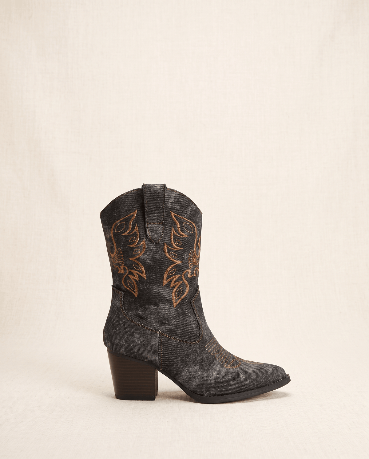Side view of a single black denim-look boot with golden embroidery and pointed toe