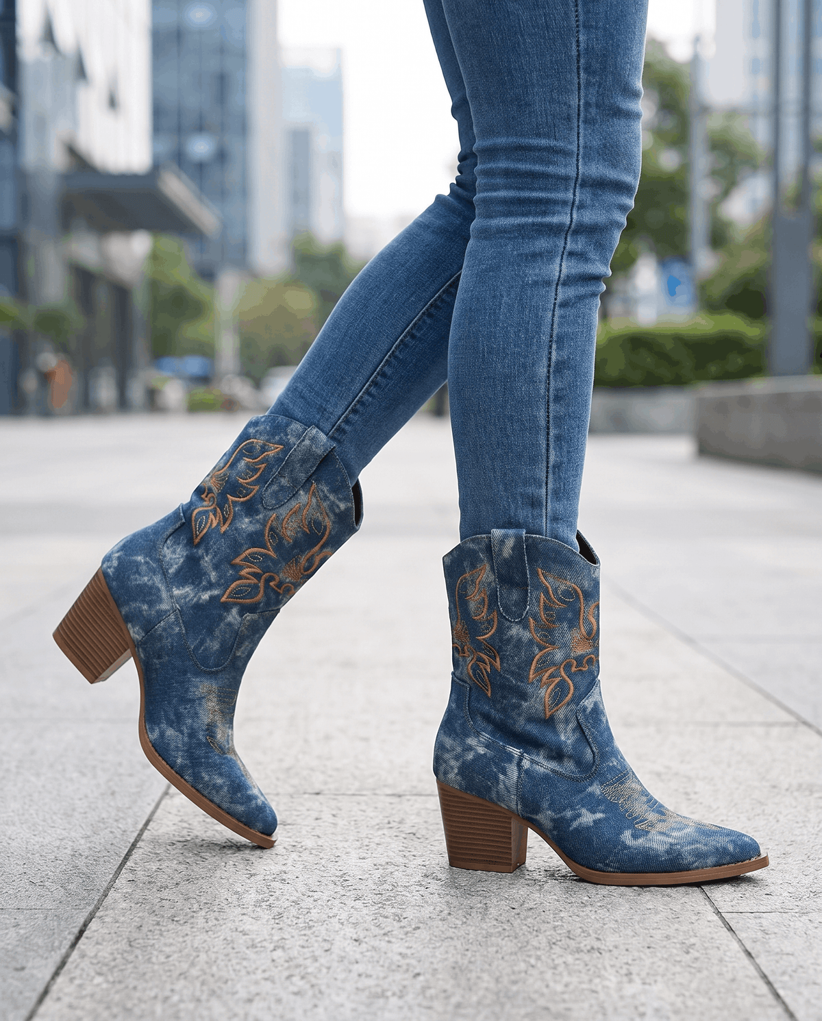 Legs in blue jeans and embroidered blue boots with block heels on a city sidewalk