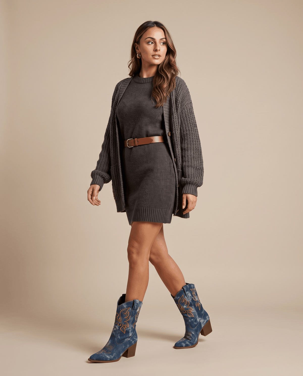 Woman in dark knit dress and cardigan wearing blue embroidered boots on a tan backdrop