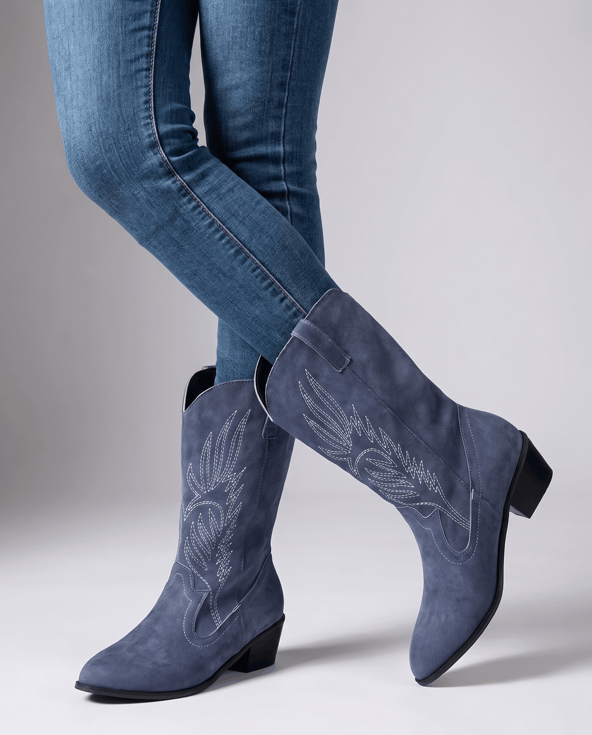 Studio shot of blue jeans worn with embroidered mid-calf suede boots and pointed toes