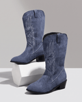 Pair of women's embroidered suede cowboy boots in navy blue with block heel on white pedestal