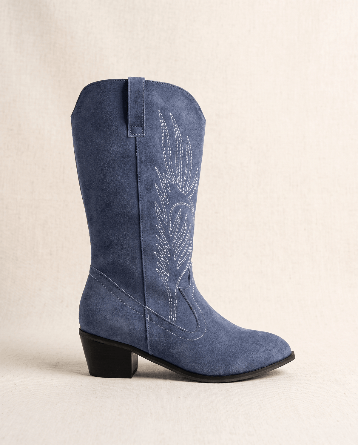 Three-quarter view of a navy blue suede boot showing pointed toe and embroidered shaft