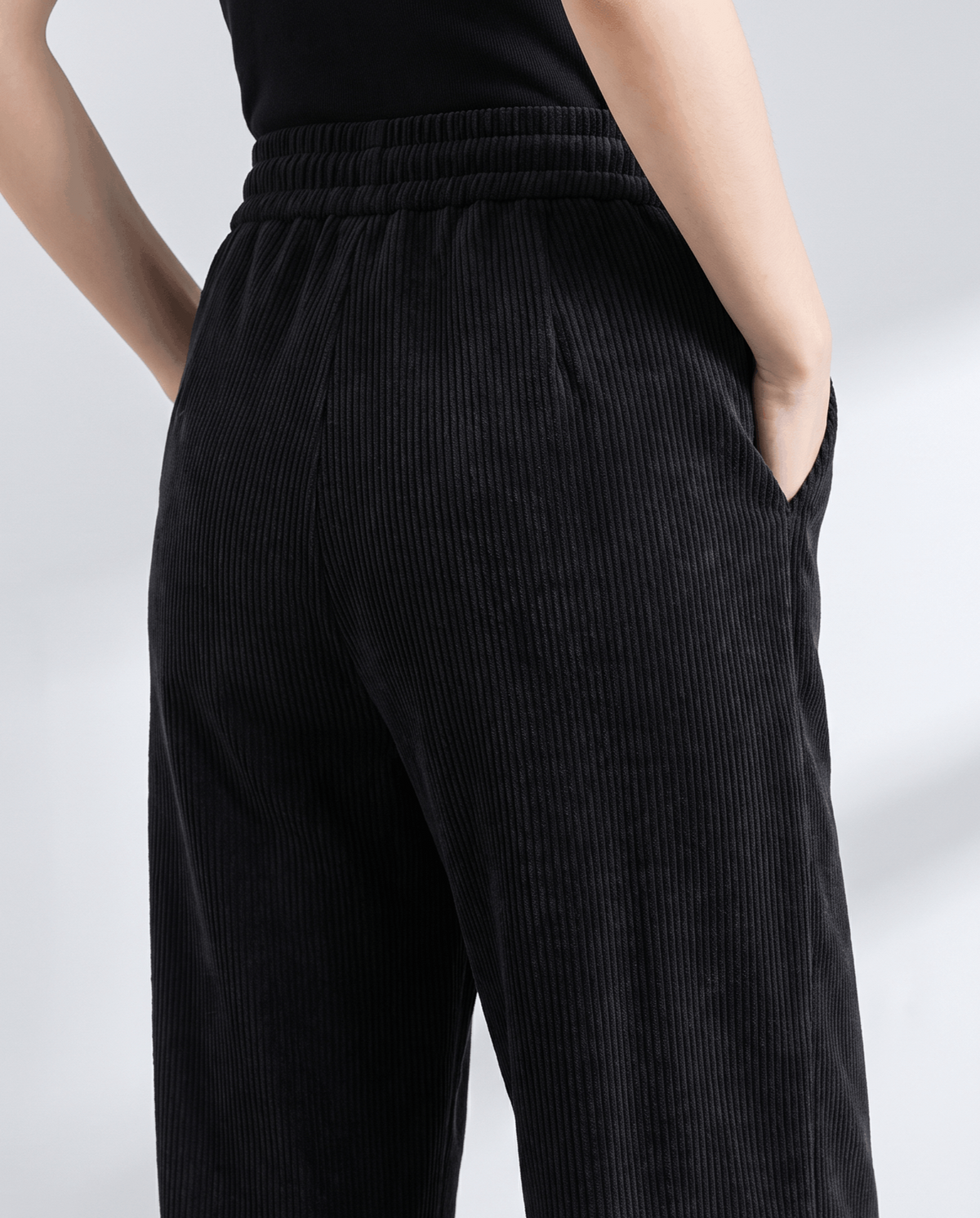 Back close-up of black ribbed trousers with the elastic waistband and a hand in the side pocket