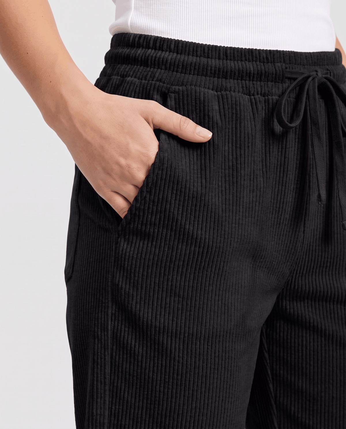 Close-up of black wide-rib corduroy with a drawstring waistband and hand in the side pocket