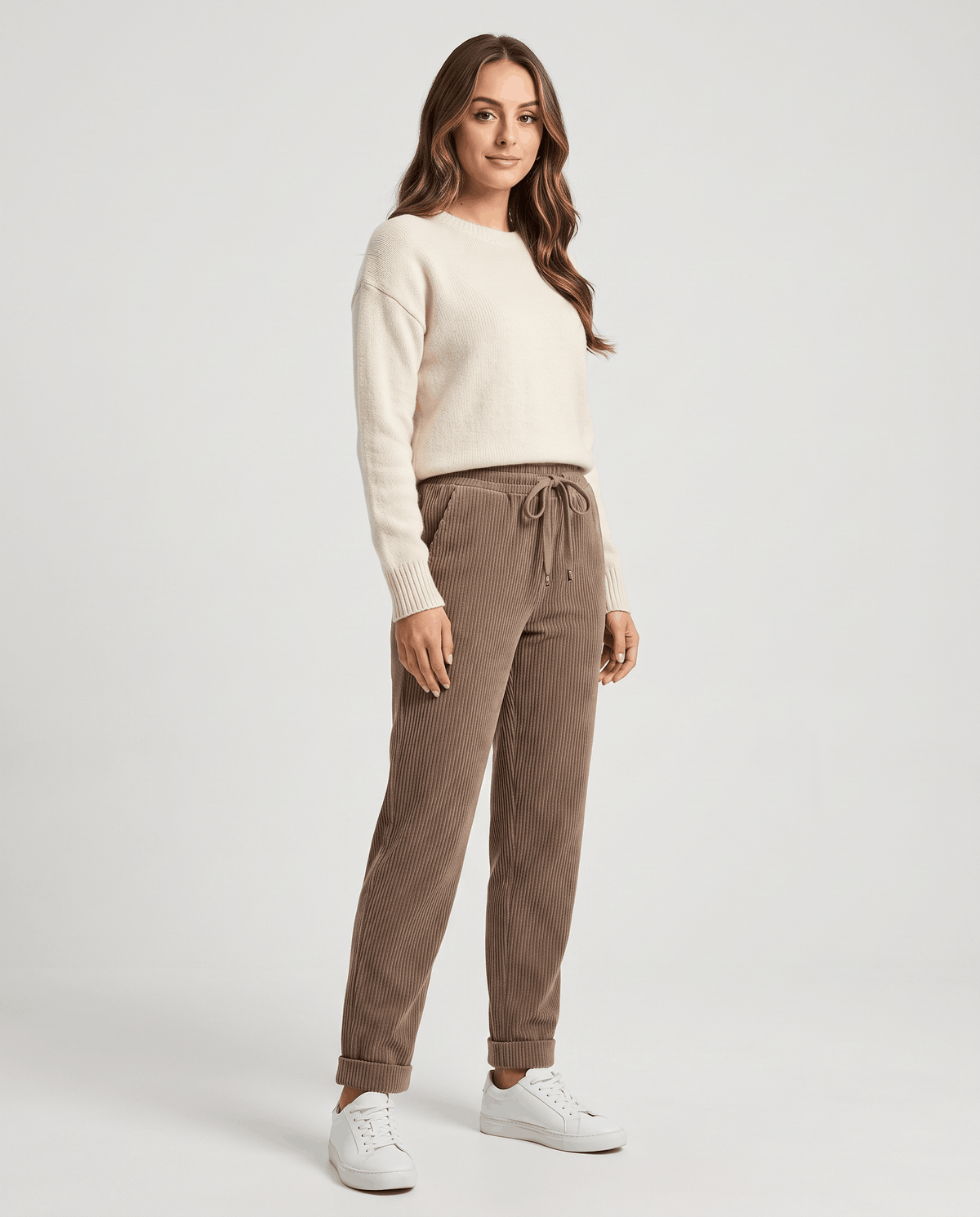 Model in taupe ribbed trousers styled with a cream knit sweater and white sneakers