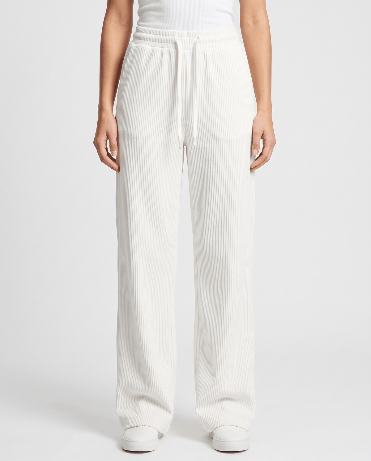 Front view of ivory wide-leg corduroy trousers with a drawstring waist and white sneakers