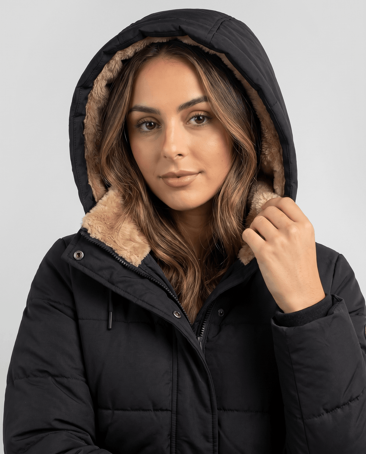 Model wearing the camel fleece-lined hood up on a black parka