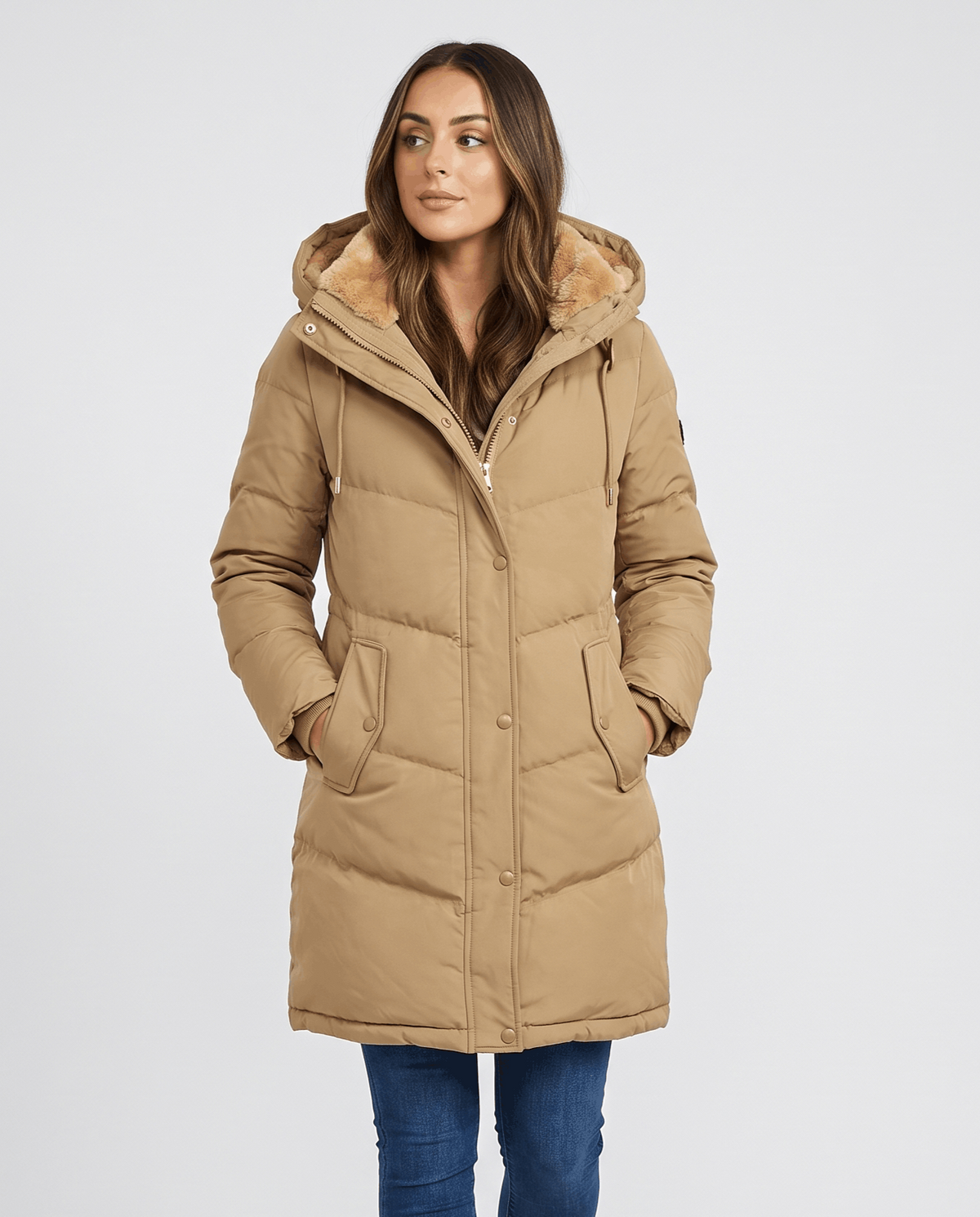 Woman in camel long quilted parka with fleece hood lining and blue jeans