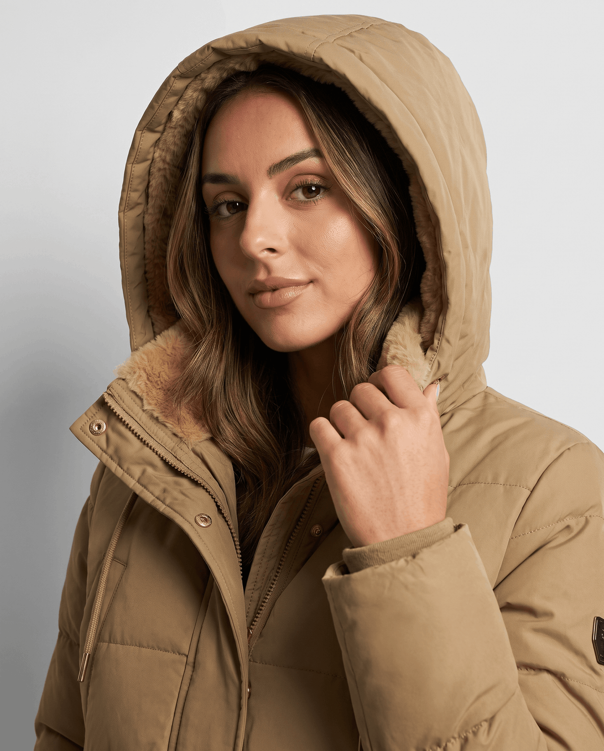 Model holding the fleece-lined hood up on a camel parka