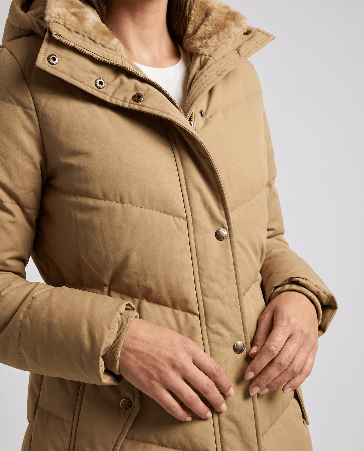 Close-up of camel parka snap placket with hands at the hem